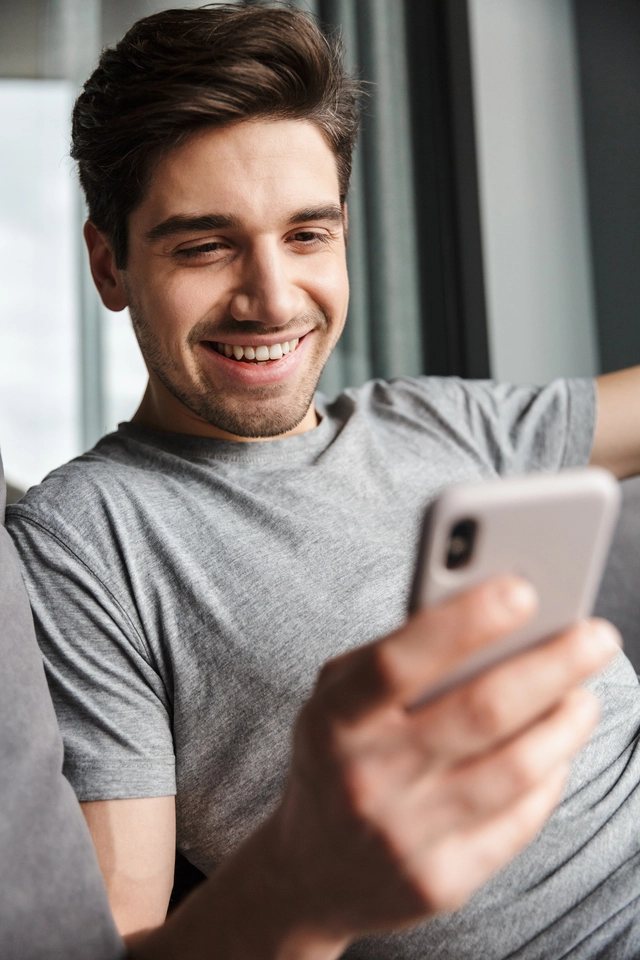 Joven sonriendo mientras observa su móvil